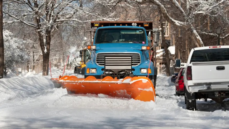 A large blue snow plow truck clearing a snow-covered residential street, ensuring safe winter roads and driveways.